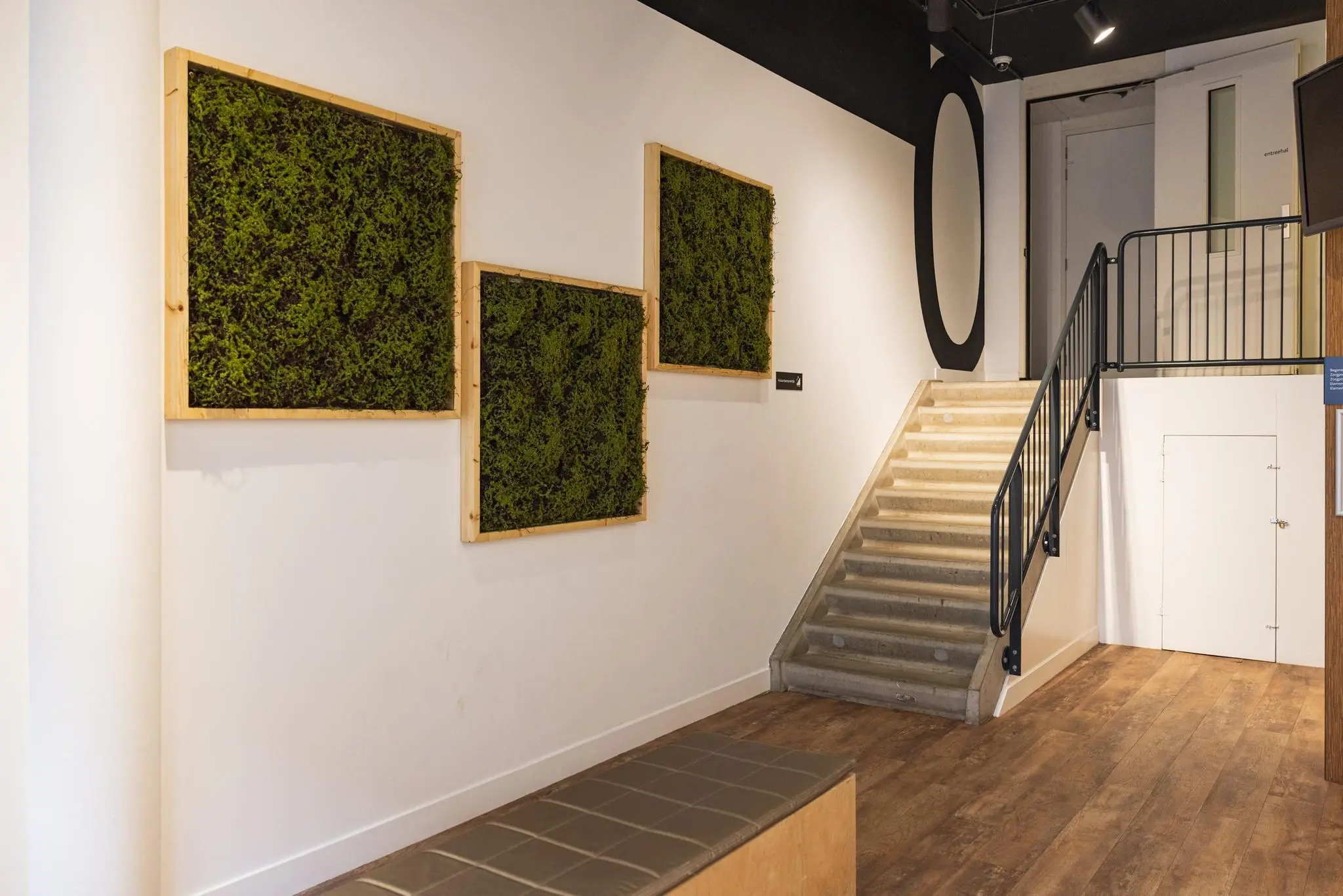 Hal met houten vloer, een trap naar boven en drie groene mospanelen aan de witte muur.