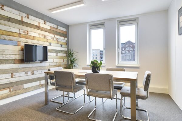 Vergaderruimte met houten wand, moderne grijze stoelen, houten tafel en uitzicht op het Middenburcht-gebouw.