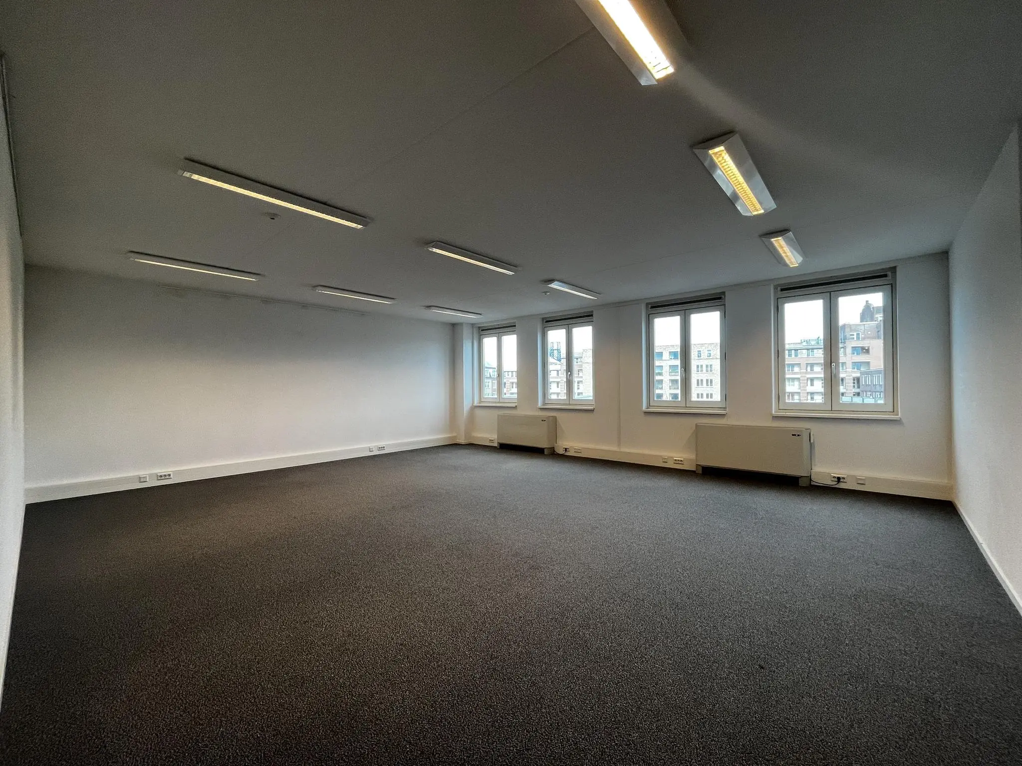 Lege kantoorruimte in het gebouw Middenburcht met meerdere ramen en uitzicht op omliggende bebouwing.