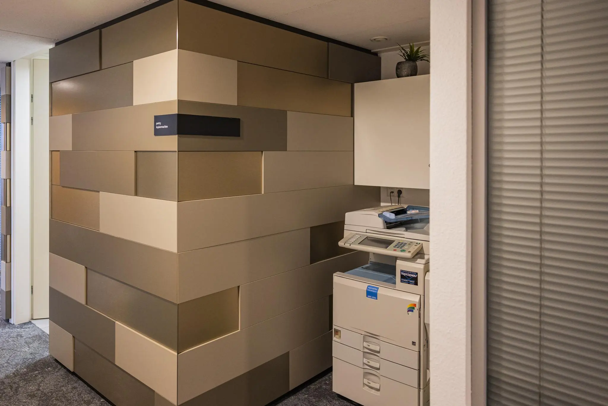 Een kopieerruimte in kantoorpand Middenburcht met een printer en moderne wandbekleding in diverse goud- en beigetinten.
