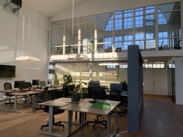 Modern kantoorinterieur aan het Gedempt Hamerkanaal met grote ramen, bureaus en computers in een open werkruimte.