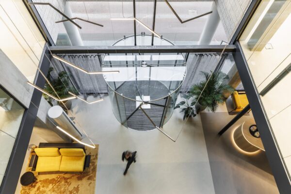 Moderne entreehal van Catharijnesingel met glazen draaideur, designverlichting en gele zitmeubels, van bovenaf gezien.