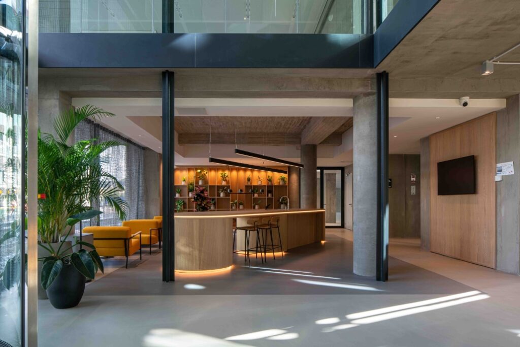Moderne en sfeervolle ontvangst- of lobbyruimte aan de Catharijnesingel met een houten balie, plantenwand en gele zitbanken.