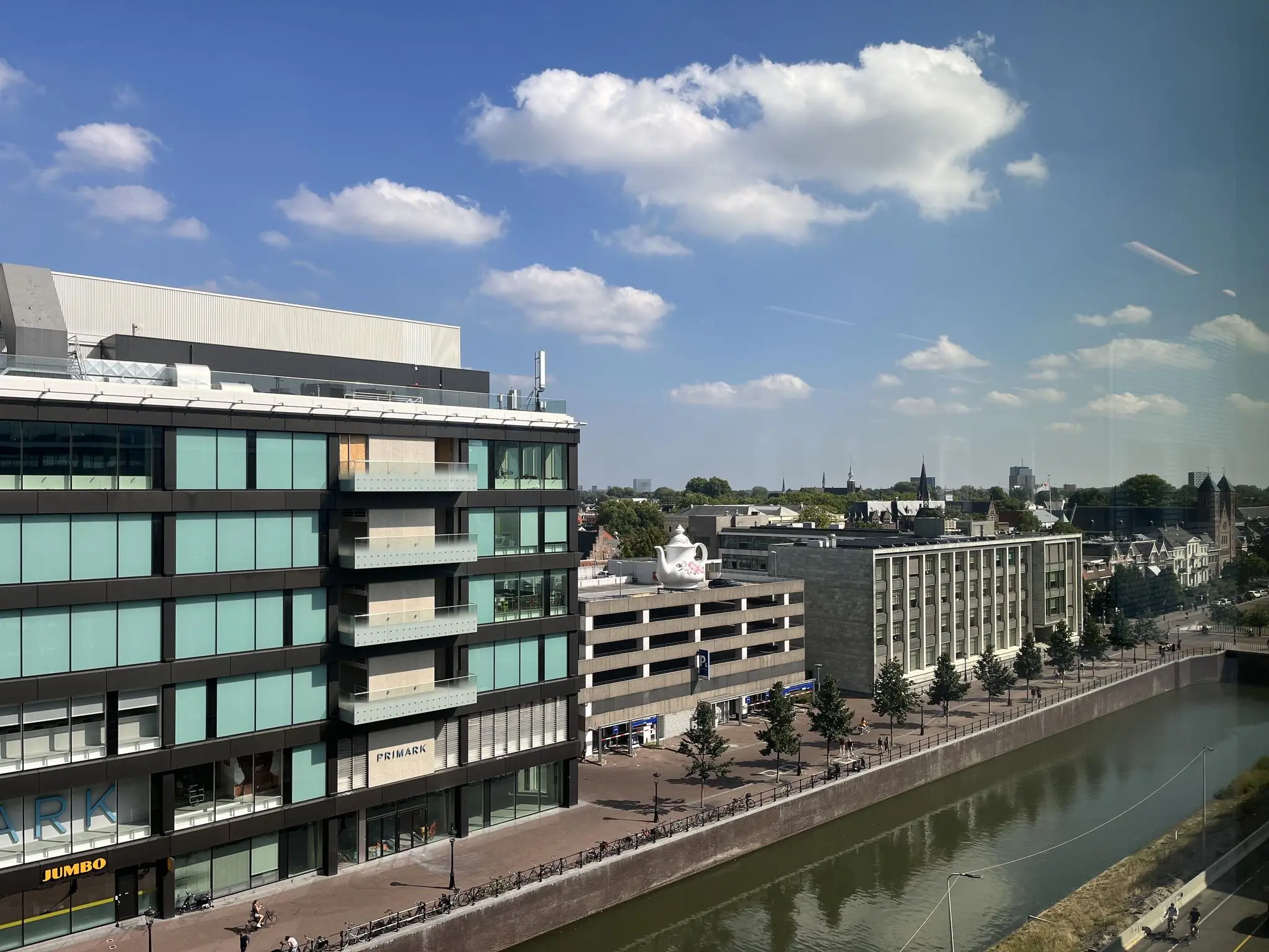 Uitzicht op de Catharijnesingel in Utrecht met moderne gebouwen, waaronder Primark en Jumbo, langs het water onder een blauwe lucht.