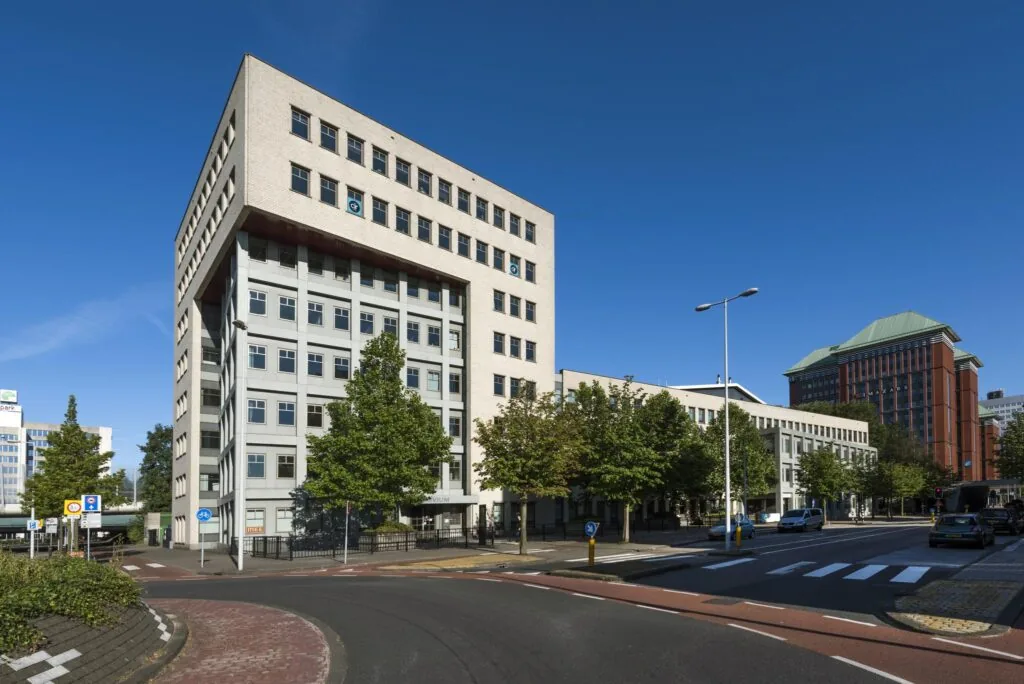 Hoekpand aan de Derkinderenstraat in Amsterdam met meerdere kantoorgebouwen en een boomrijke straat op een zonnige dag.
