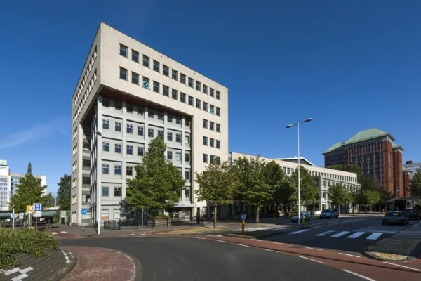 Hoekpand aan de Derkinderenstraat in Amsterdam met meerdere kantoorgebouwen en een boomrijke straat op een zonnige dag.