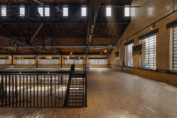 Bovenverdieping van de industriële hal aan de Leidseweg, ingericht als expositieruimte met houten vloer en hangende fotopanelen.