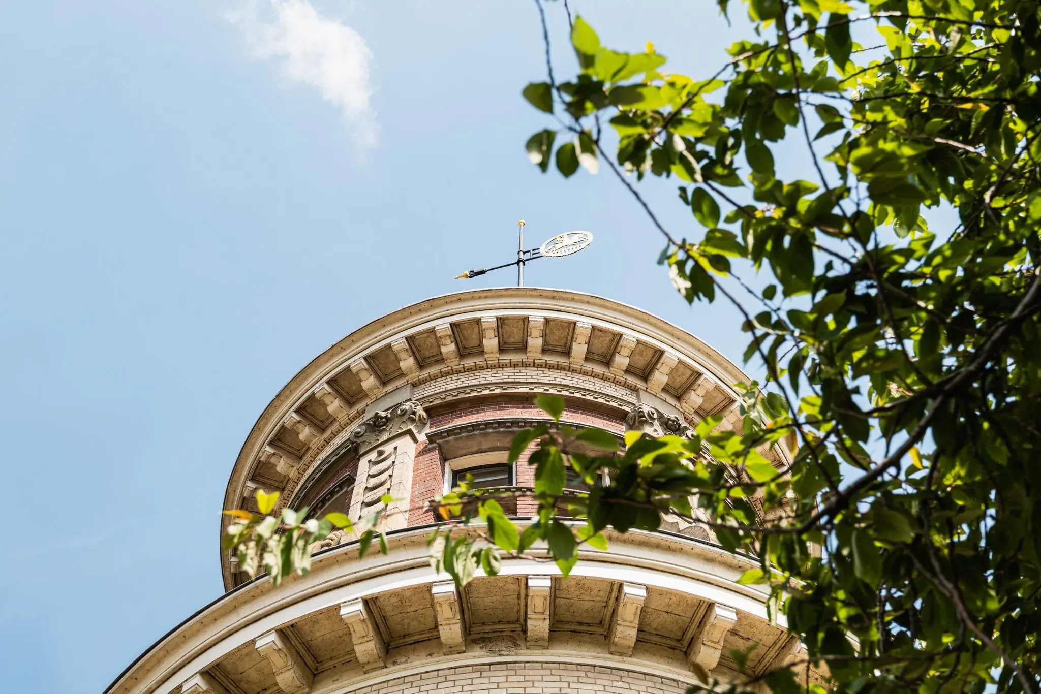 Bovenaanzicht van een ronde toren aan de Leidseweg met klassieke geveldetails en een windvaan, deels omgeven door groene bladeren.