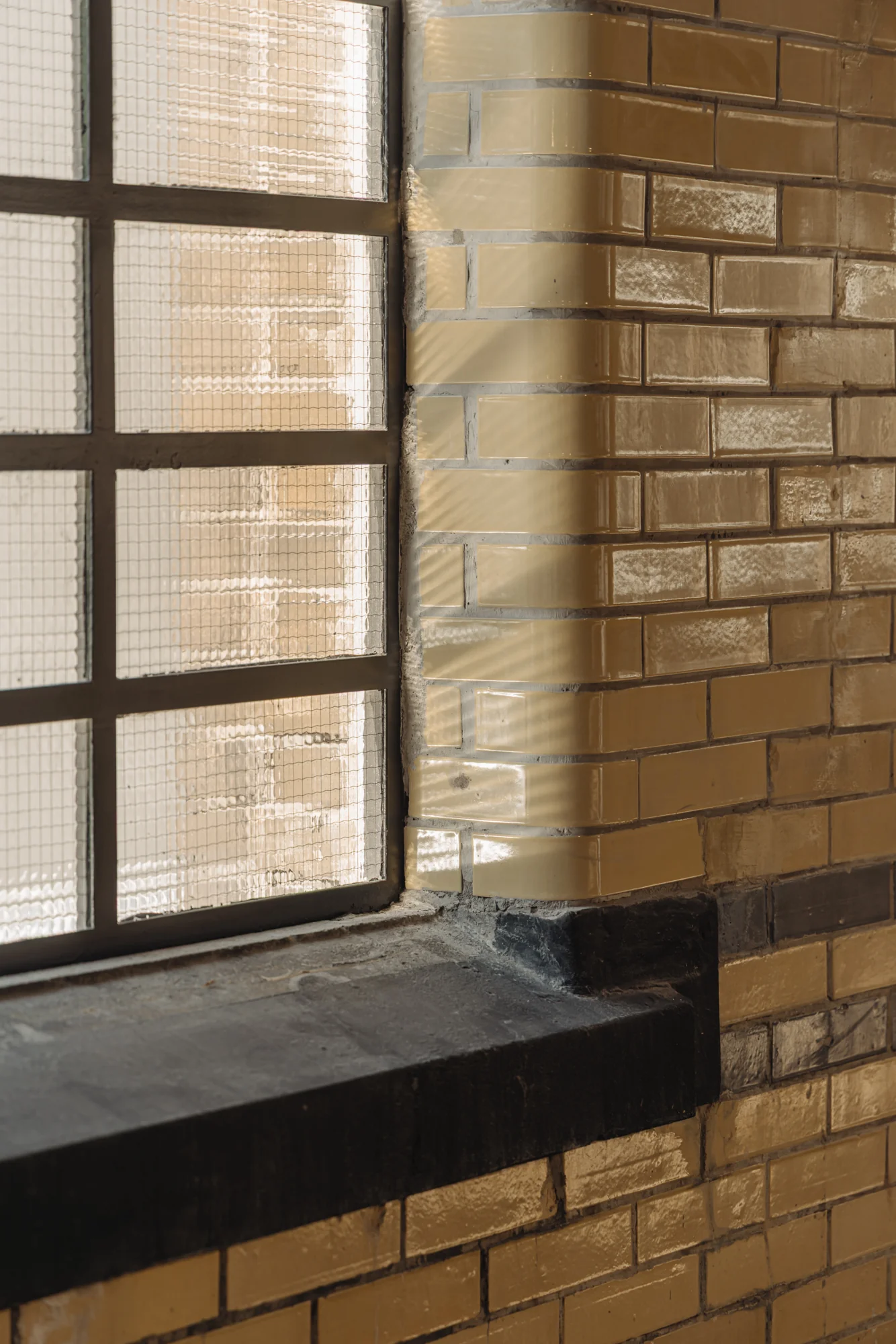 Detail van een binnenmuur met glanzende gele bakstenen en een roosterraam op Leidseweg.