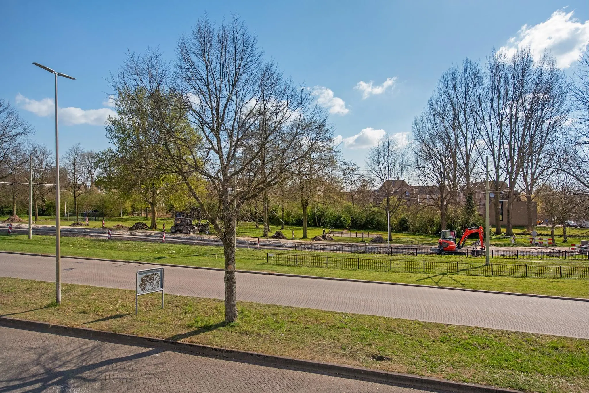 Wegenwerkzaamheden aan de Lagosweg met een graafmachine en afgezette rijstroken in een groene, boomrijke omgeving.