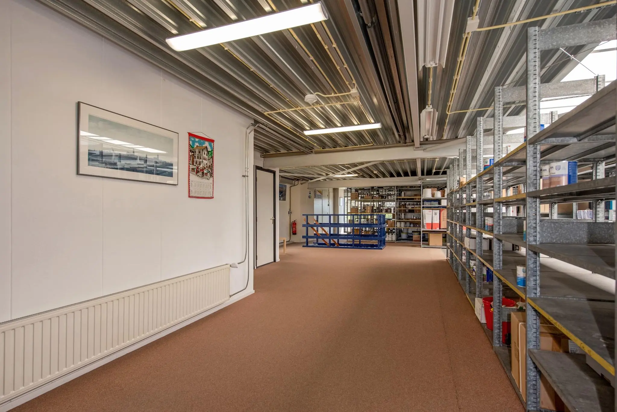 Opslagruimte met metalen stellingkasten, een open trap en wanddecoratie aan de linkerkant.