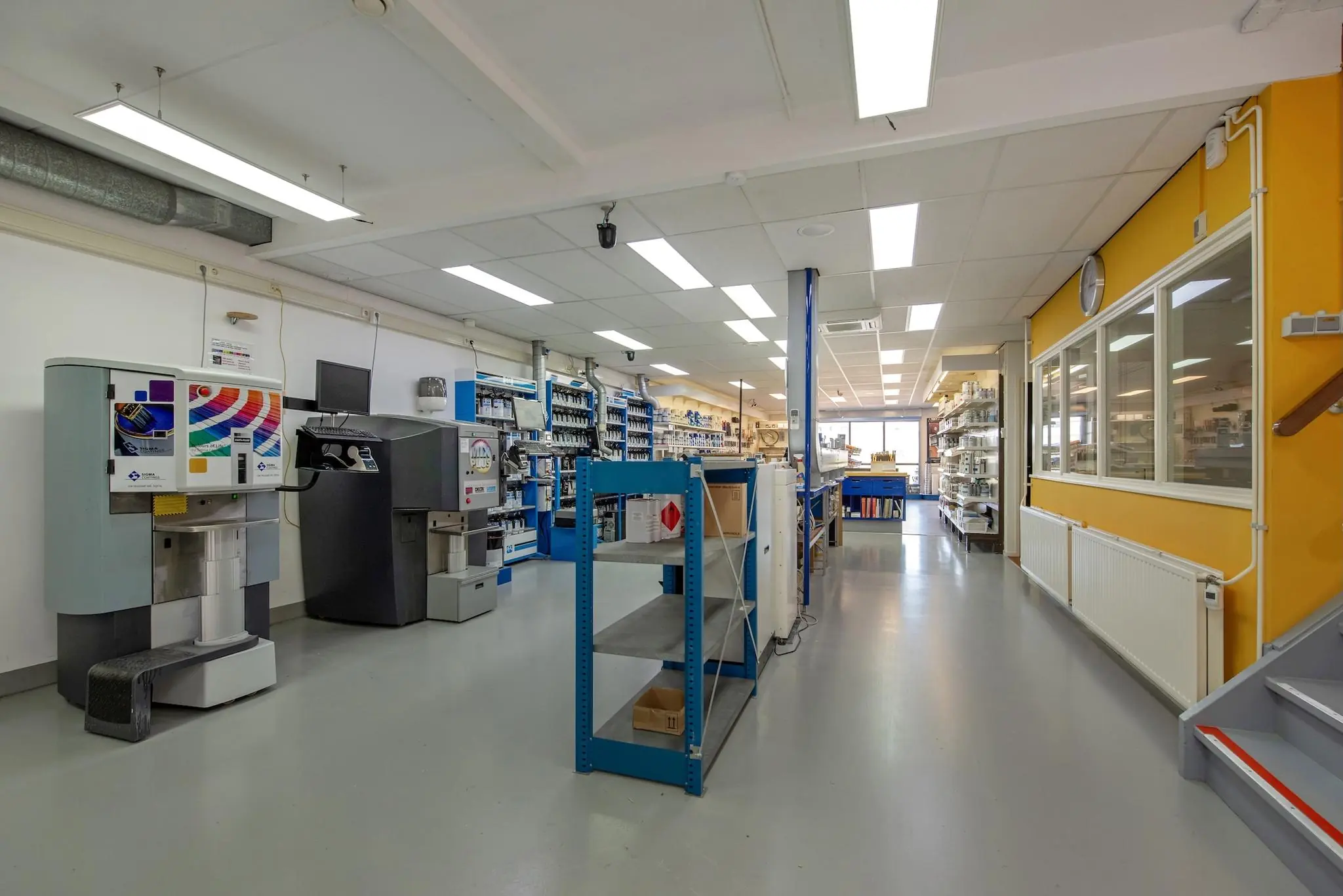 Interieur van een verf- en onderhoudsmaterialenwinkel met kleurmengmachines, stellingen en werkruimte aan de Lagosweg.
