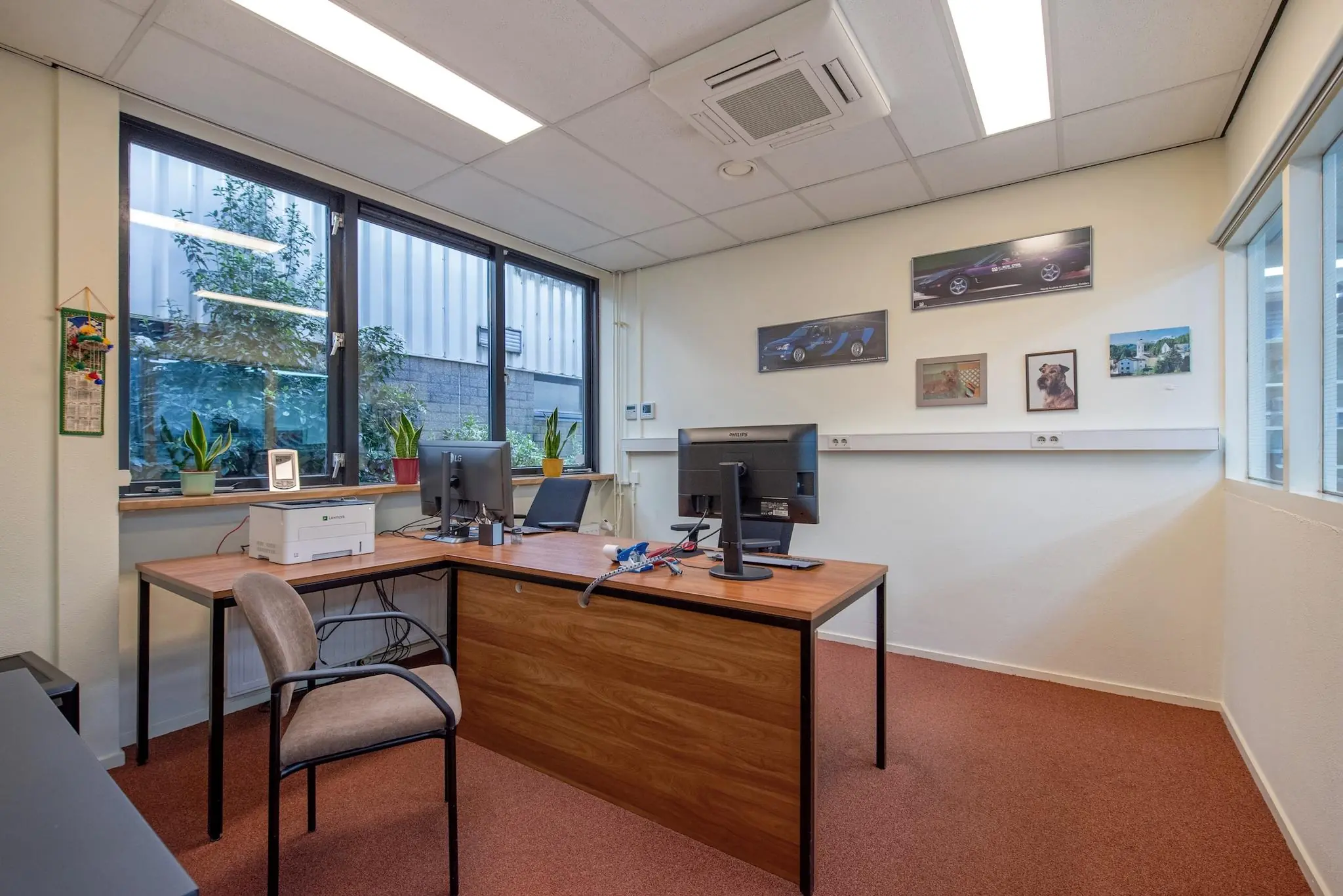 Modern kantoor met twee bureaus, computerschermen, kamerplanten en decoratieve wandfoto’s aan de Lagosweg.