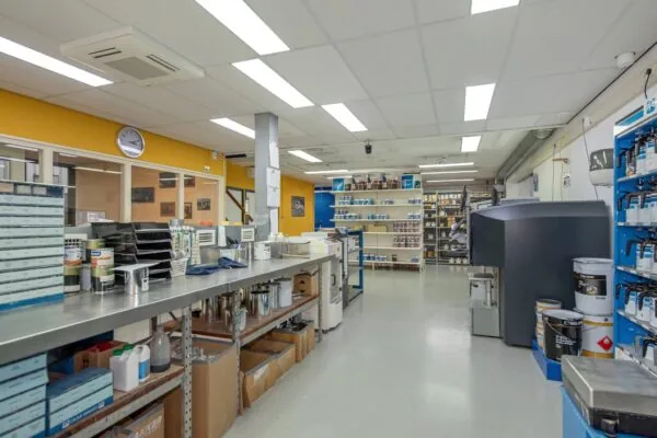 Een goed verlichte werkruimte in een verflaboratorium of mengruimte met verfpotten, gereedschap en opslagrekken.