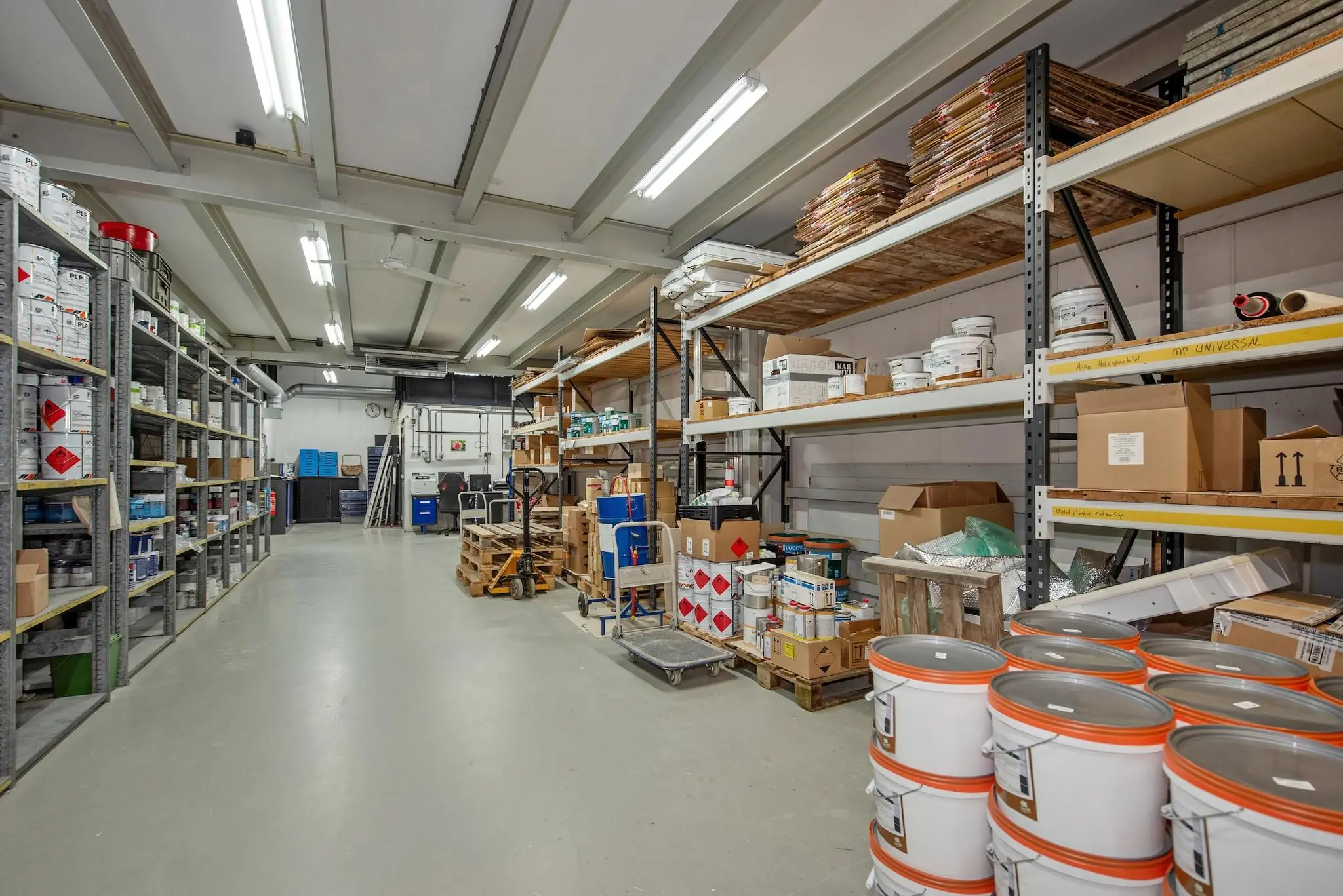 Opgeruimde opslagruimte aan de Lagosweg met stellingen vol verfblikken, dozen en bouwmaterialen.