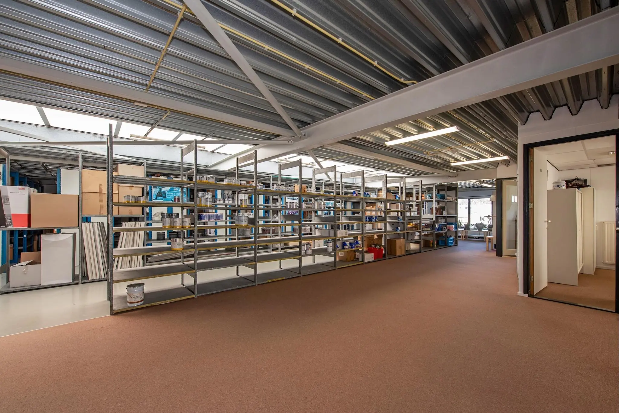 Magazijnruimte aan de Lagosweg met metalen stellingen gevuld met diverse producten en dozen.