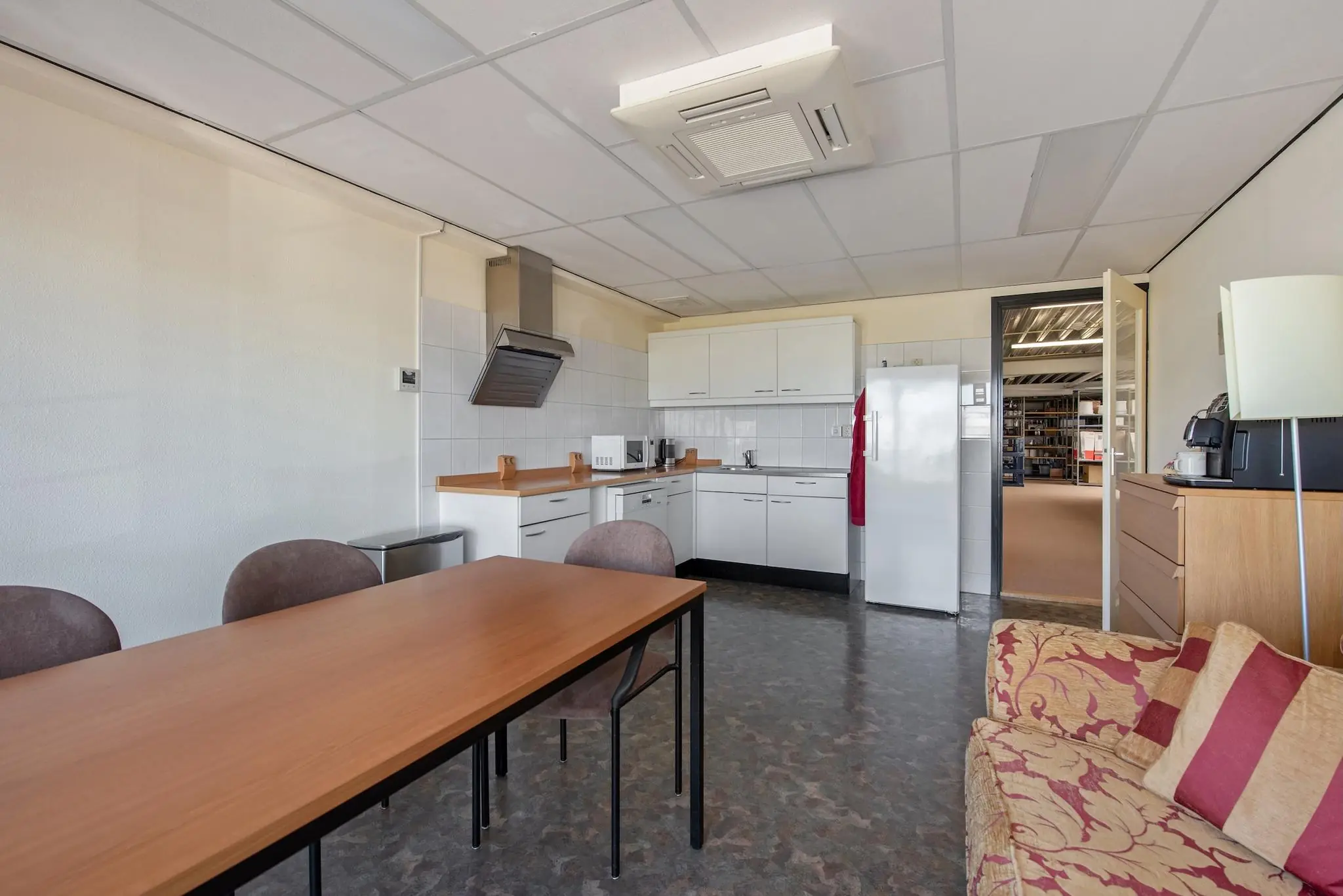 Bedrijfskantine met een eenvoudige witte keuken, een eettafel en een zitbank aan de Lagosweg.