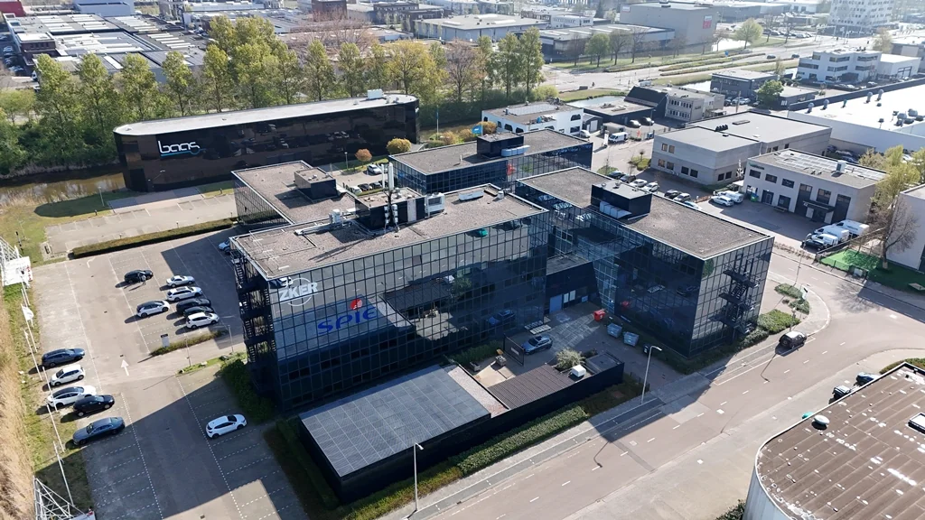 Aerial view of the SPIE office building on Essebaan in a business park surrounded by other commercial buildings and parked cars.