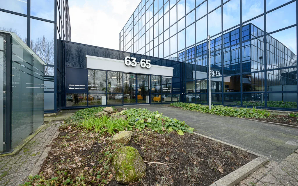 Modern office building at Essebaan 63-65 with reflective glass facade and landscaped entrance path.