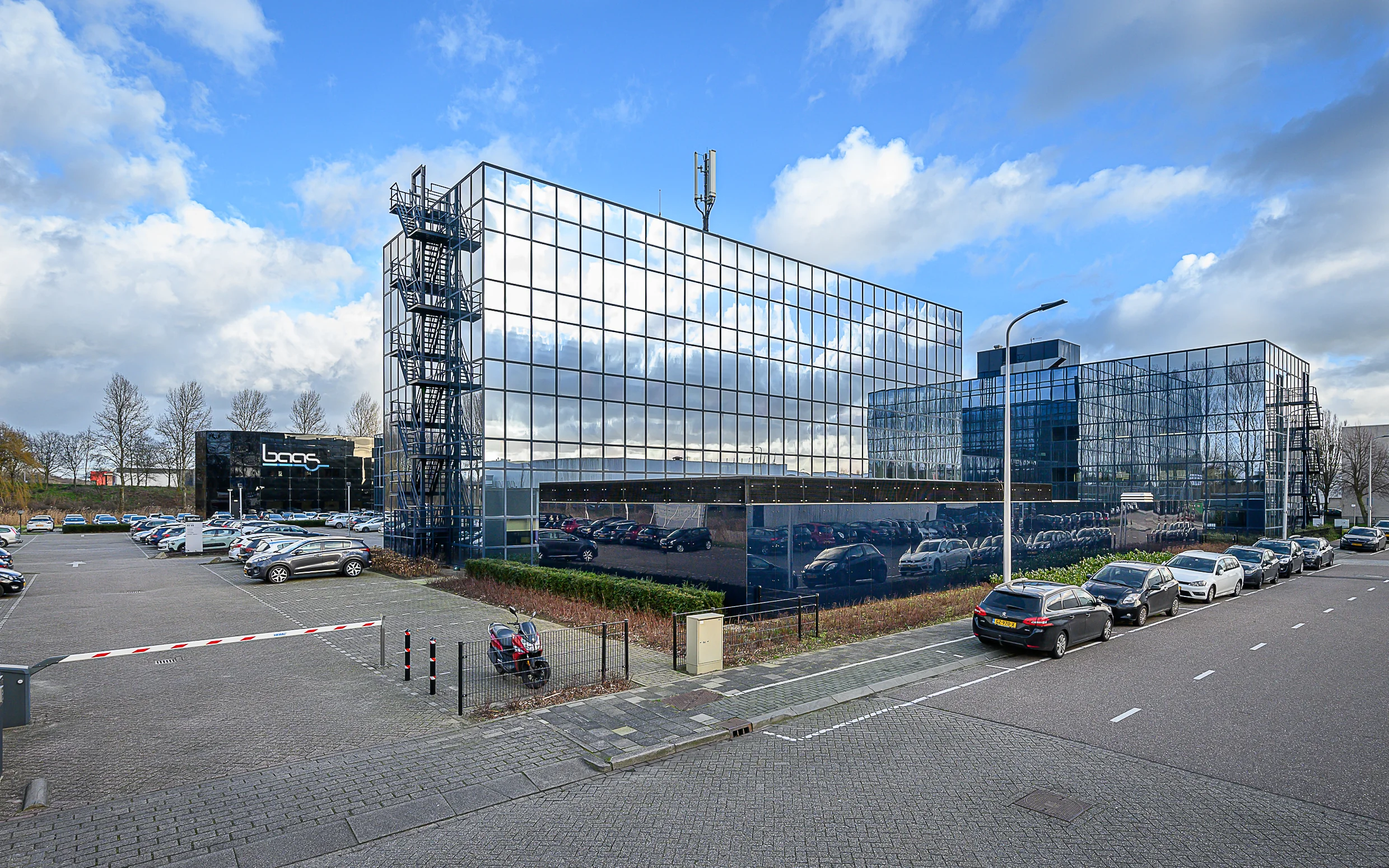 Modern glass office buildings with the company name "Baas" and a parking lot on Essebaan street.