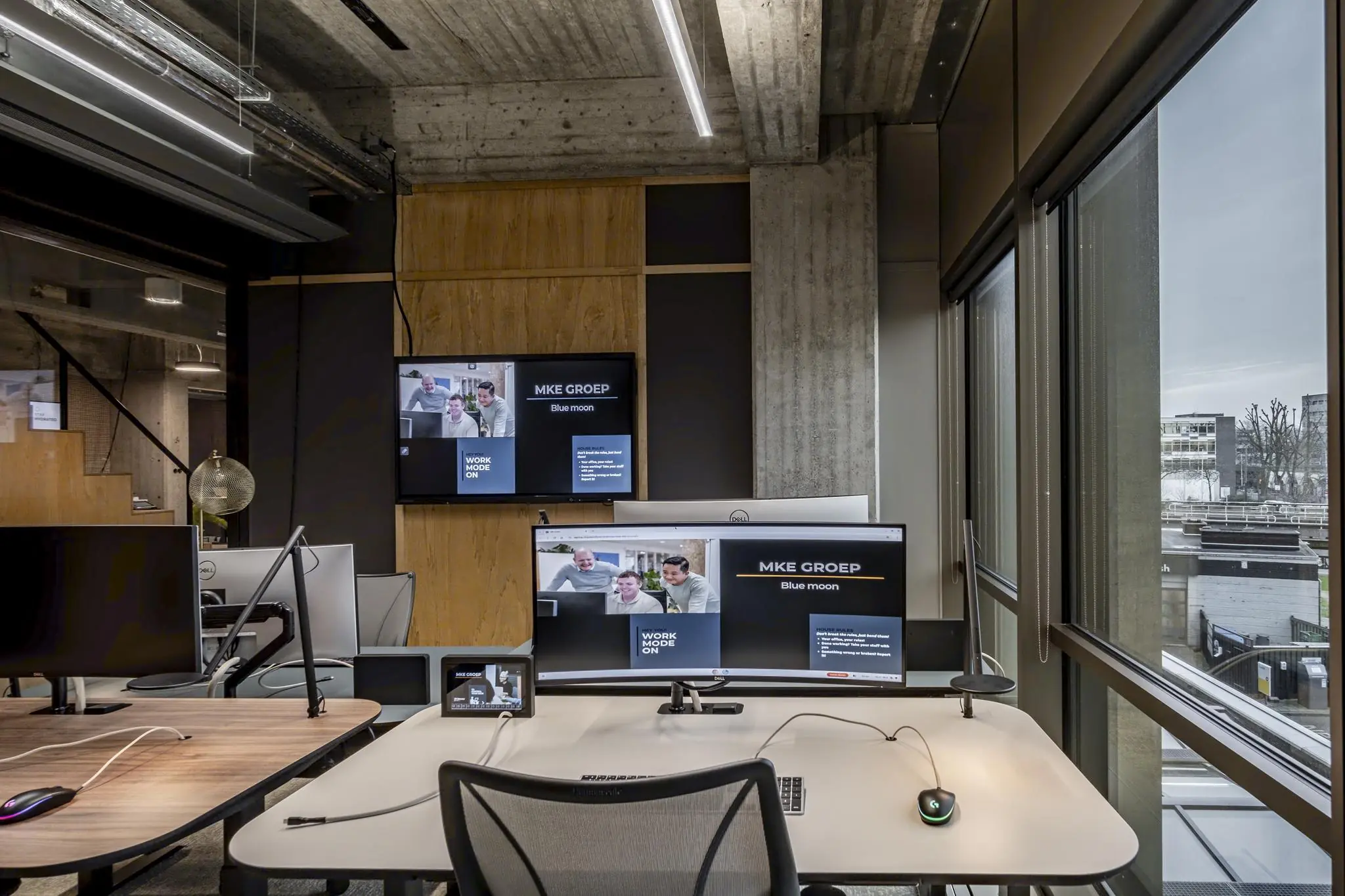 Modern kantoorinterieur met werkplekken, grote beeldschermen en uitzicht op Hofplein in Rotterdam.