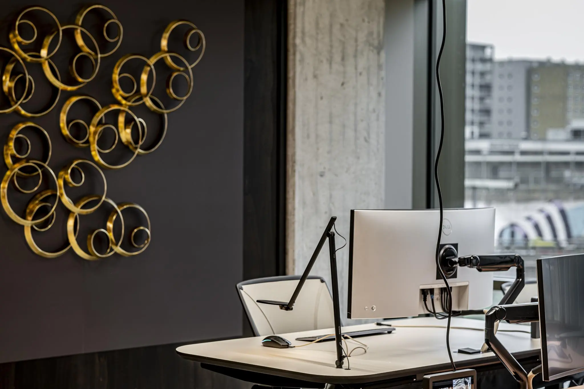 Modern kantoorinterieur met een strakke werkplek, een kunstwerk van gouden ringen aan de muur en uitzicht op Hofplein in Rotterdam.