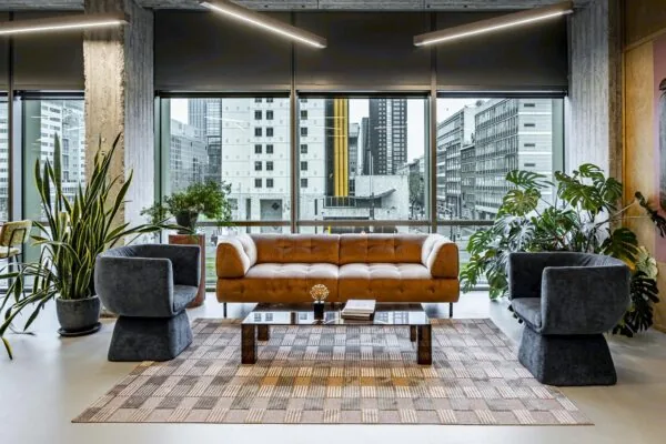 Modern ingerichte loungehoek met een bruine bank, grijze fauteuils, kamerplanten en uitzicht op Hofplein in Rotterdam.