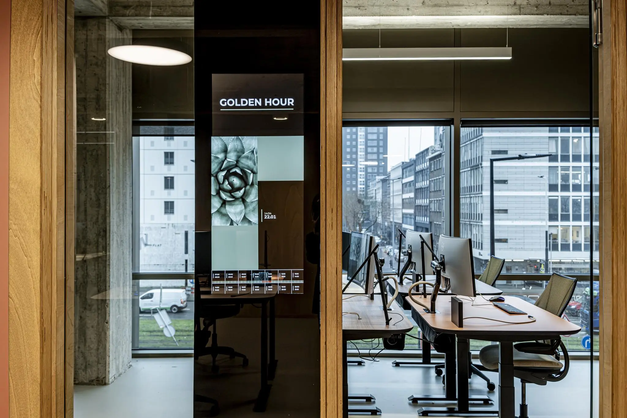 Modern kantoorinterieur aan het Hofplein met werkplekken, een digitaal scherm met "Golden Hour" en uitzicht op de stad.
