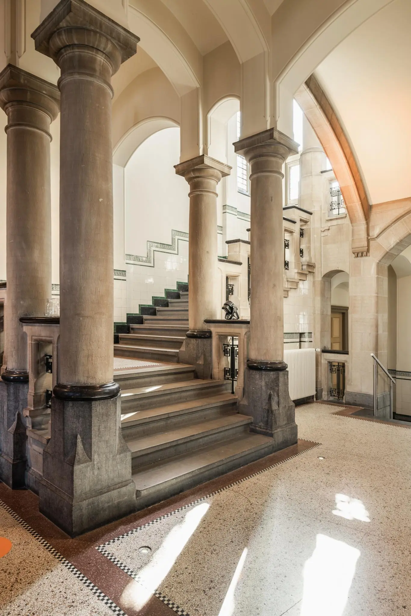 Monumentaal trappenhuis met stenen zuilen, natuurstenen trap en betegelde wanden in een pand aan de Leidseweg.
