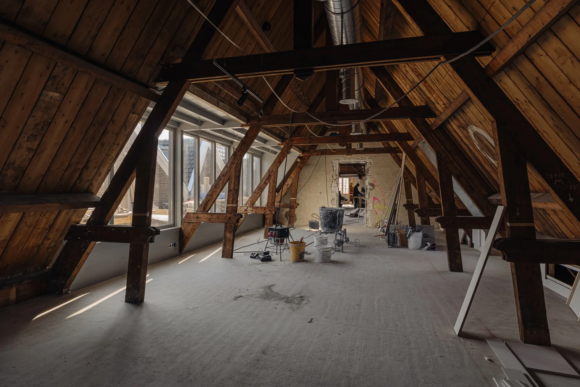 Zolderruimte van een oud pand aan de Leidseweg in verbouwing, met zichtbare houten spanten en bouwmaterialen.