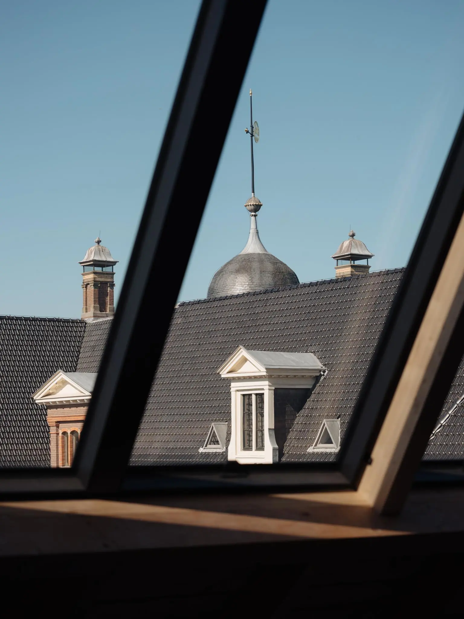 Uitzicht vanaf een zolderraam op het dak en de torenspits van een historisch gebouw aan de Leidseweg.