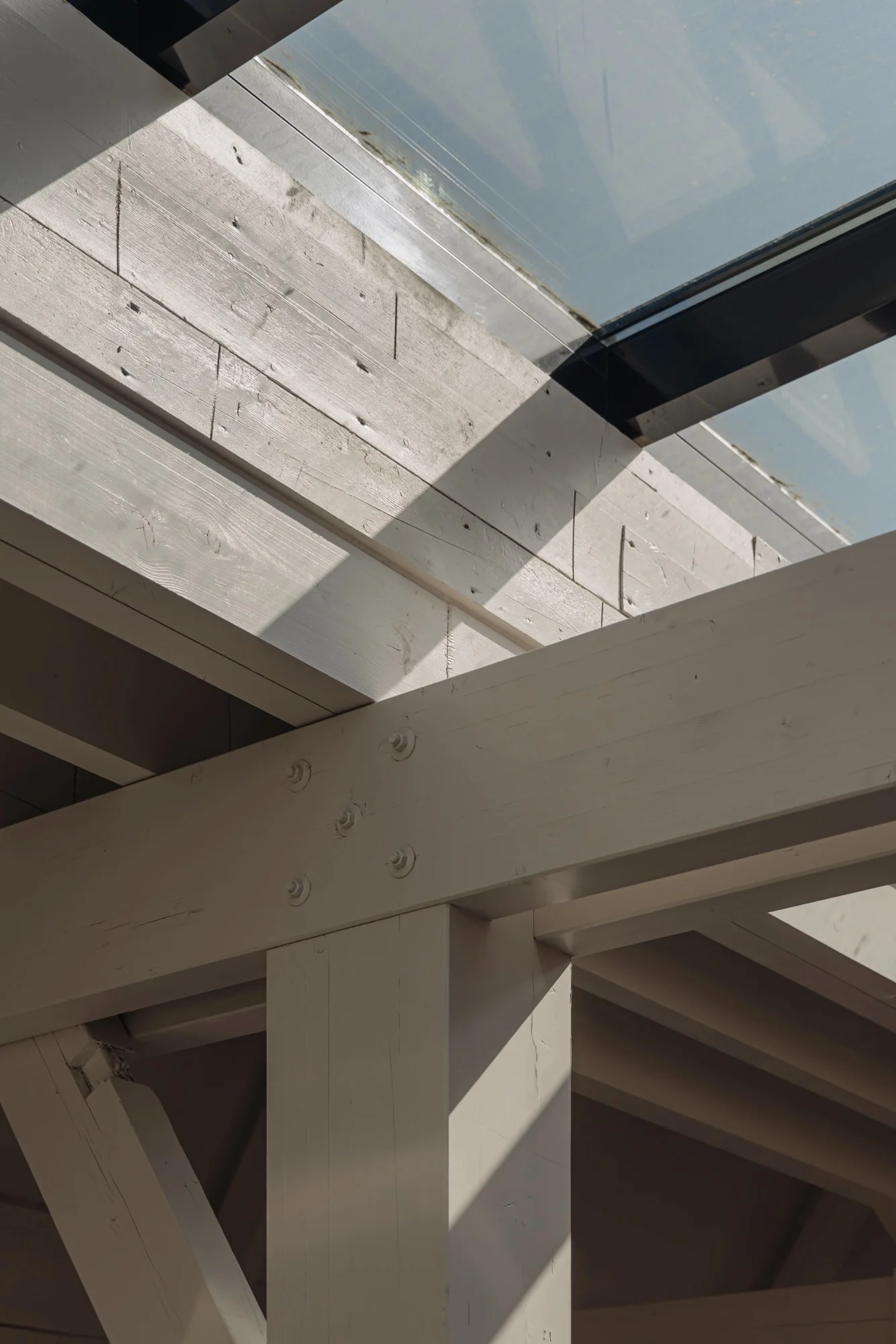 Houten draagconstructie onder een glazen dak op Leidseweg, belicht door zonlicht dat schaduwen werpt.