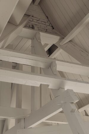 Houten dakconstructie met witgeschilderde balken en zichtbare bakstenen muur aan de Leidseweg.