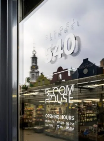 Glasdeur met het adres Singel 540 en de naam Bloom House, met daarachter een bloemenwinkel en de Munttoren weerspiegeld in het raam.