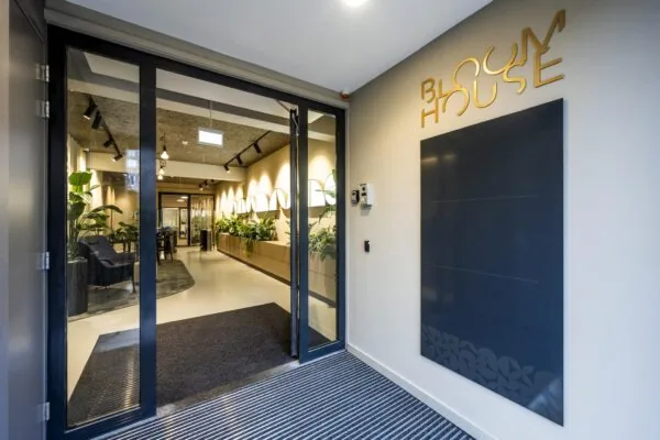 Ingang van het moderne kantoorgebouw Bloom House met glazen deuren en een sfeervol interieur vol planten.