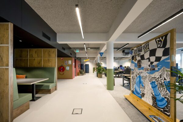 Modern kantoorinterieur met open werkplekken, een zithoek en een kleurrijke muurschildering met schaakthema en het woord "STRATEGY".
