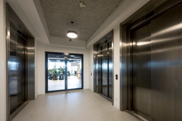 Moderne liftlobby met drie rvs-liften en glazen deuren naar een kantoorruimte aan de Singel.