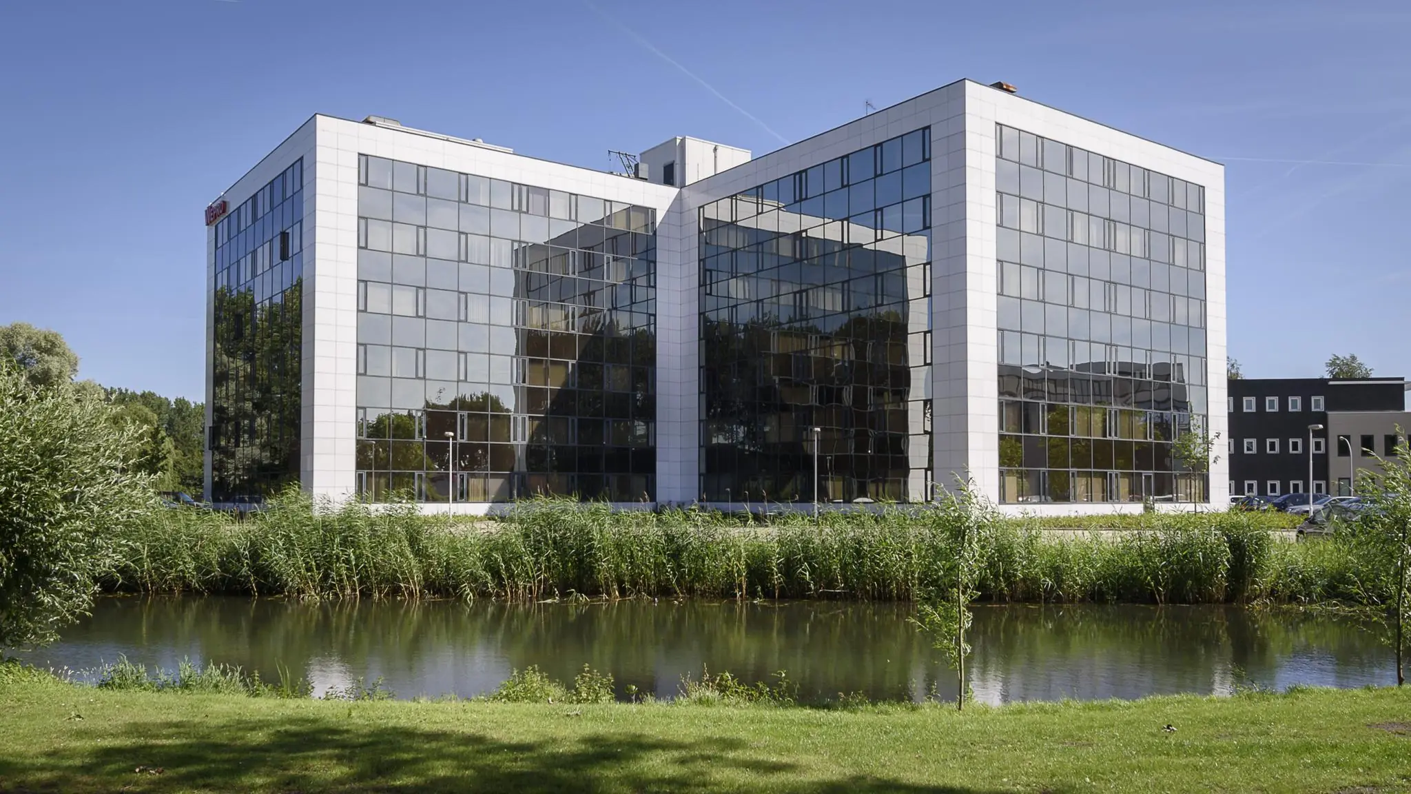 Modern kantoorgebouw aan de Cypresbaan met spiegelende gevel, gelegen aan een waterpartij.