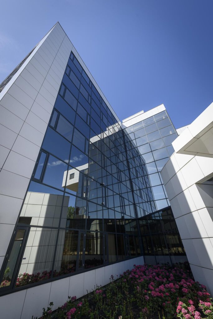 Modern kantoorgebouw aan de Cypresbaan met glazen gevel en bloemperk op de voorgrond.