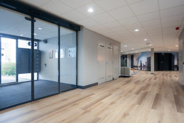 Moderne en lichte entreehal van een bedrijfsverzamelgebouw aan de Cypresbaan met houten vloer en glazen schuifdeuren.