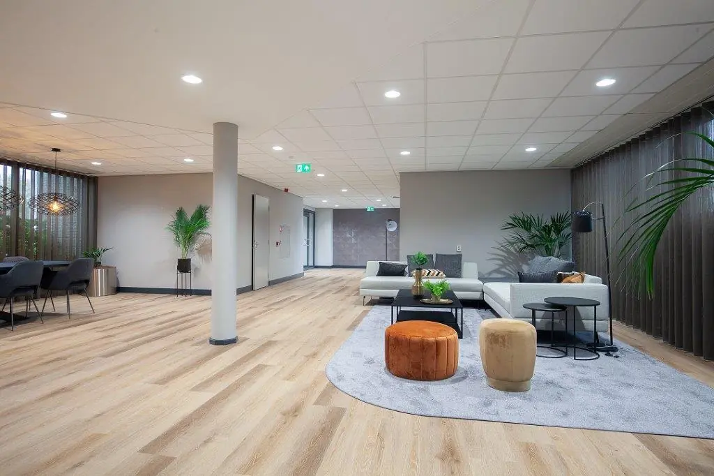 Moderne, ruim opgezette wachtruimte met lichte houten vloer, zithoeken en veel groene planten in een pand aan de Cypresbaan.