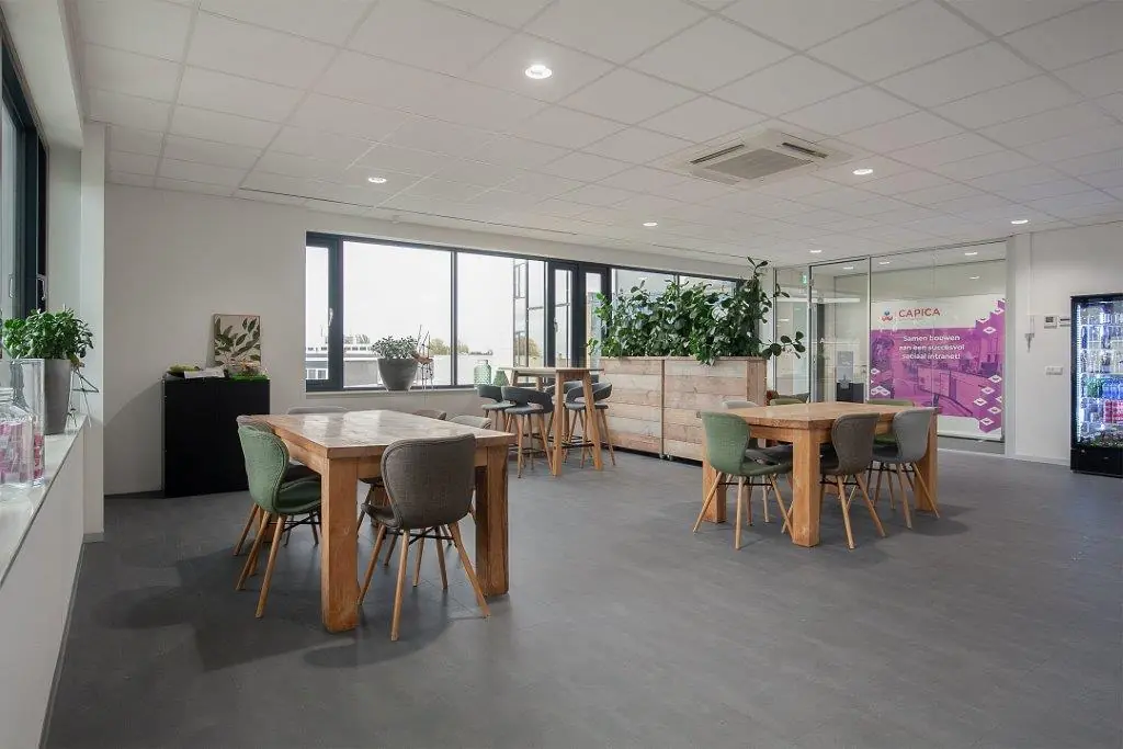 Moderne en lichte bedrijfsruimte aan de Cypresbaan met houten tafels, groene planten en glazen vergaderruimte van Capica.