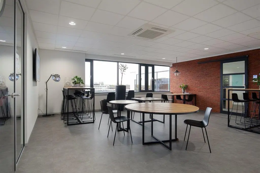 Moderne kantoorkantine met ronde en hoge tafels, industriële details en uitzicht op de Cypresbaan.