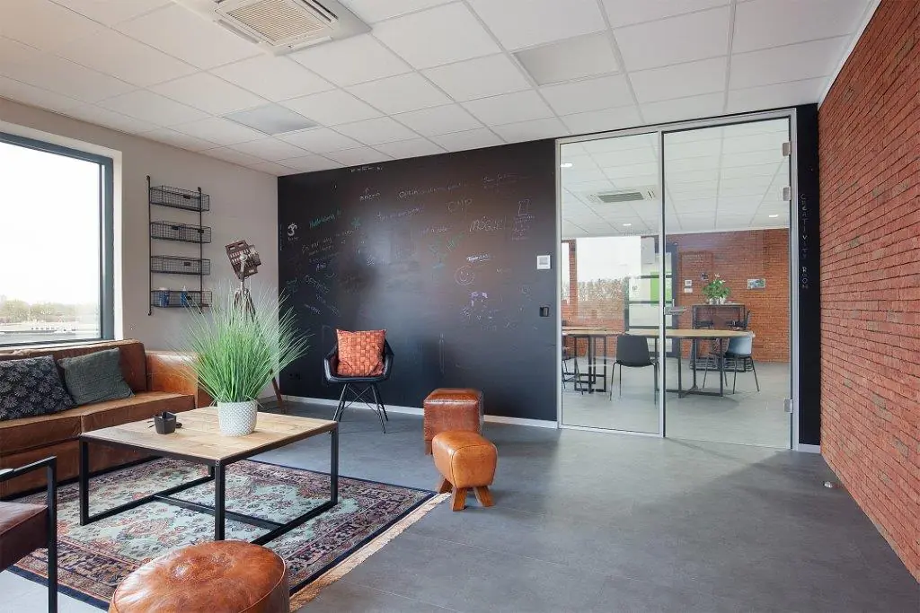 Moderne kantoorlounge met leren zitmeubels, een zwarte krijtwand en glazen vergaderruimte aan de Cypresbaan.