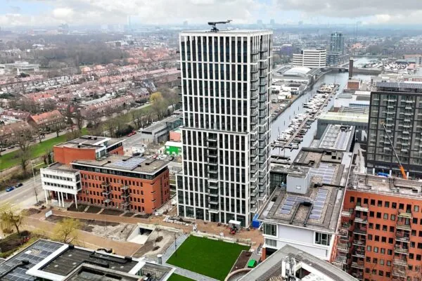 Luchtfoto van de woontoren aan het Maanplein in Den Haag, omringd door moderne gebouwen, een jachthaven en woonwijken.