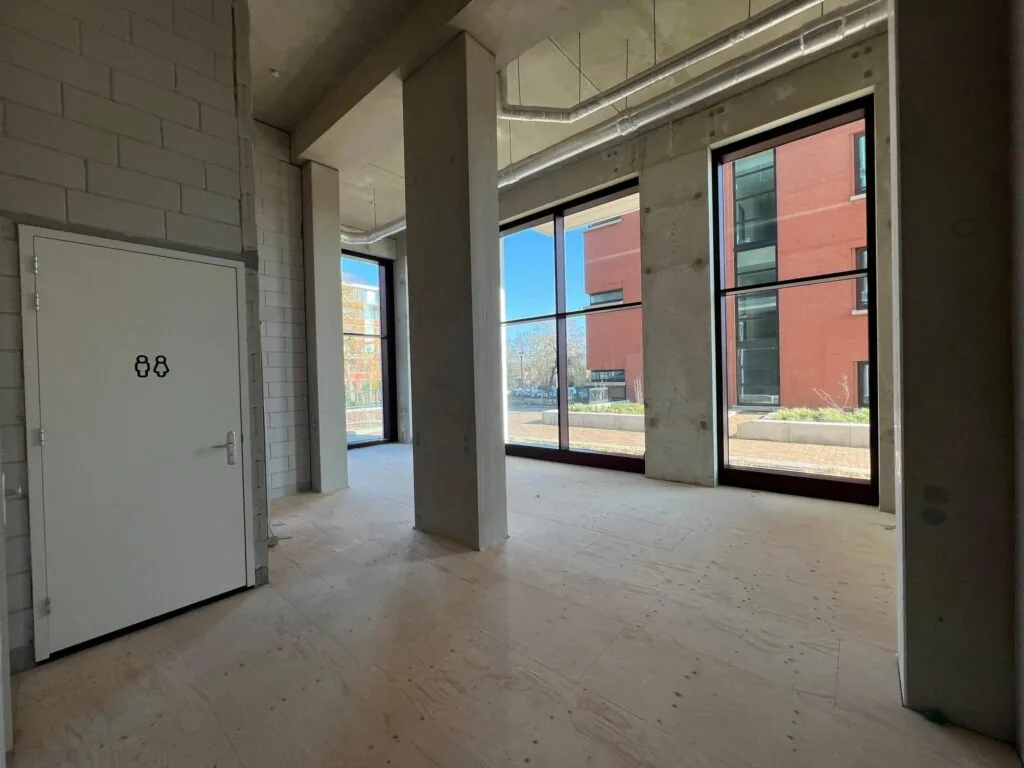 Binnenruimte aan het Maanplein met grote ramen, betonnen muren en een deur met toiletpictogram.