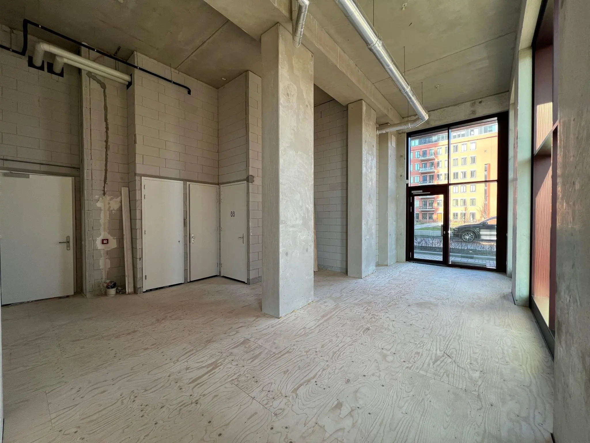 Leeg casco winkel- of bedrijfsruimte met hoge plafonds aan het Maanplein, met groot raam en uitzicht op appartementencomplex.