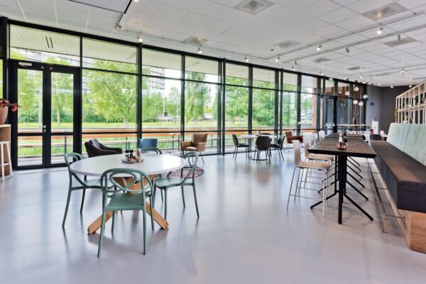 Moderne en licht ingerichte kantineruimte aan de Prof. W.H. Keesomlaan met grote ramen en uitzicht op groen.