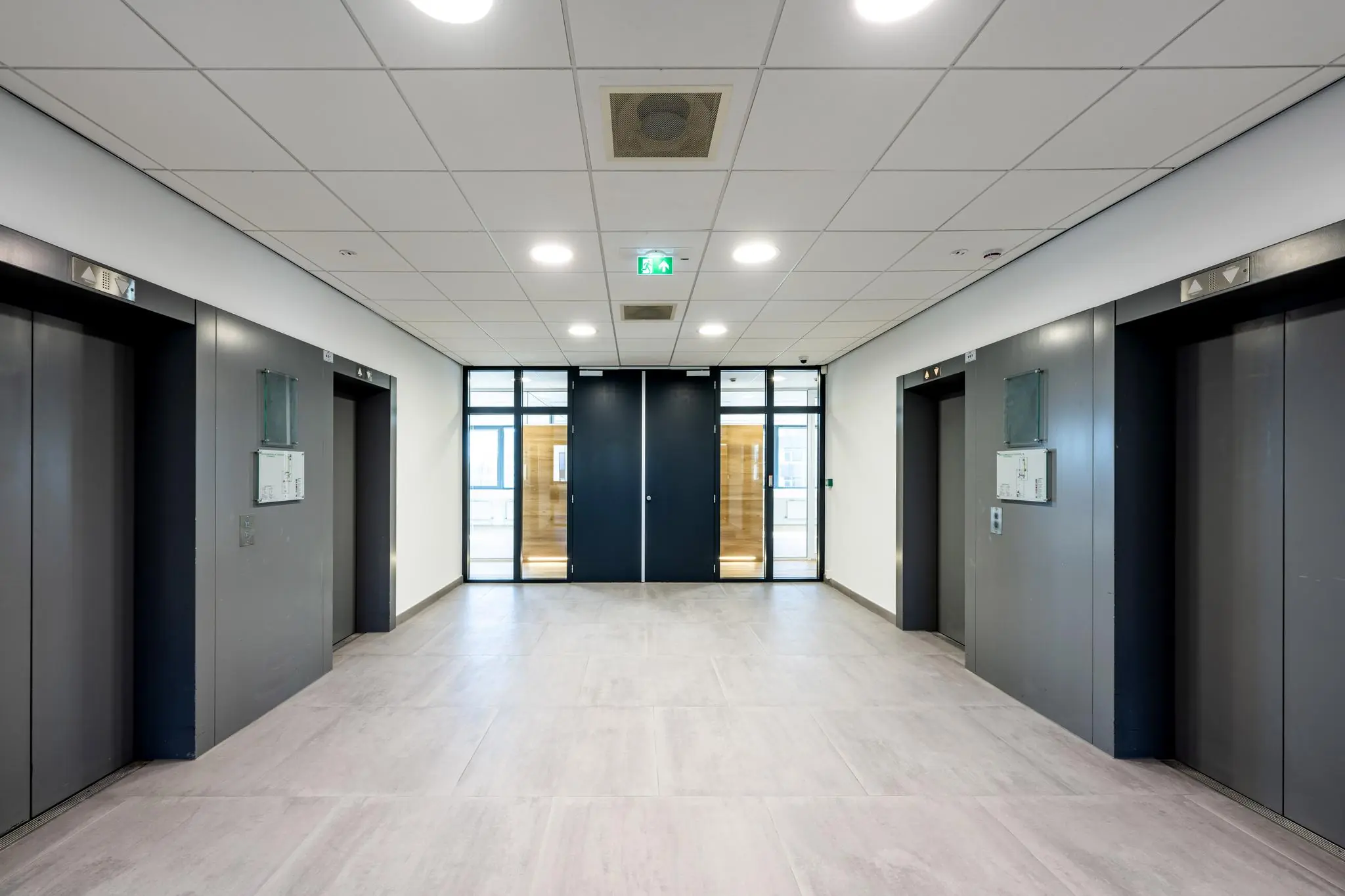 Moderne liftlobby met vier gesloten liften en een dubbele glazen deur aan het einde van de gang in een kantoorgebouw aan de Prof. W.H. Keesomlaan.