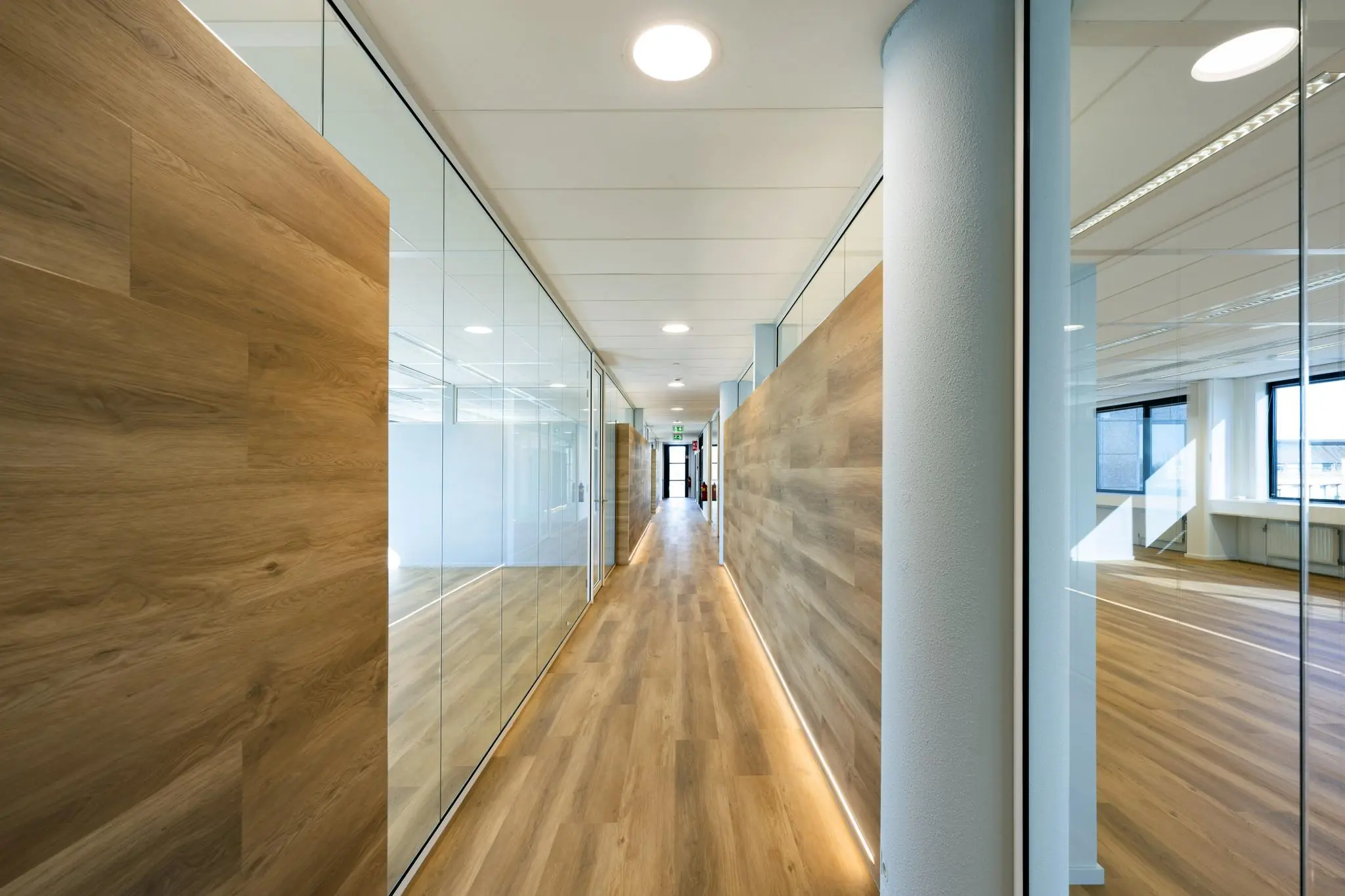Modern kantoorinterieur met een lange gang voorzien van houten vloer, glazen wanden en strakke verlichting aan de Prof. W.H. Keesomlaan.